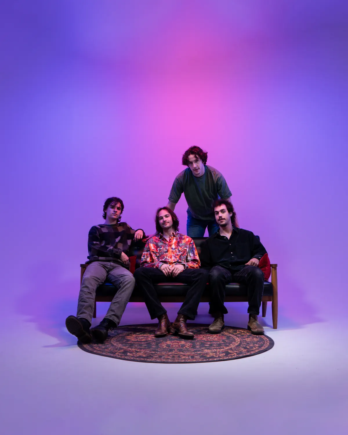 Lewis Ashe, Chris Hankey, Erik Wolstenholme and Mason Wiley on a couch under magenta studio light.