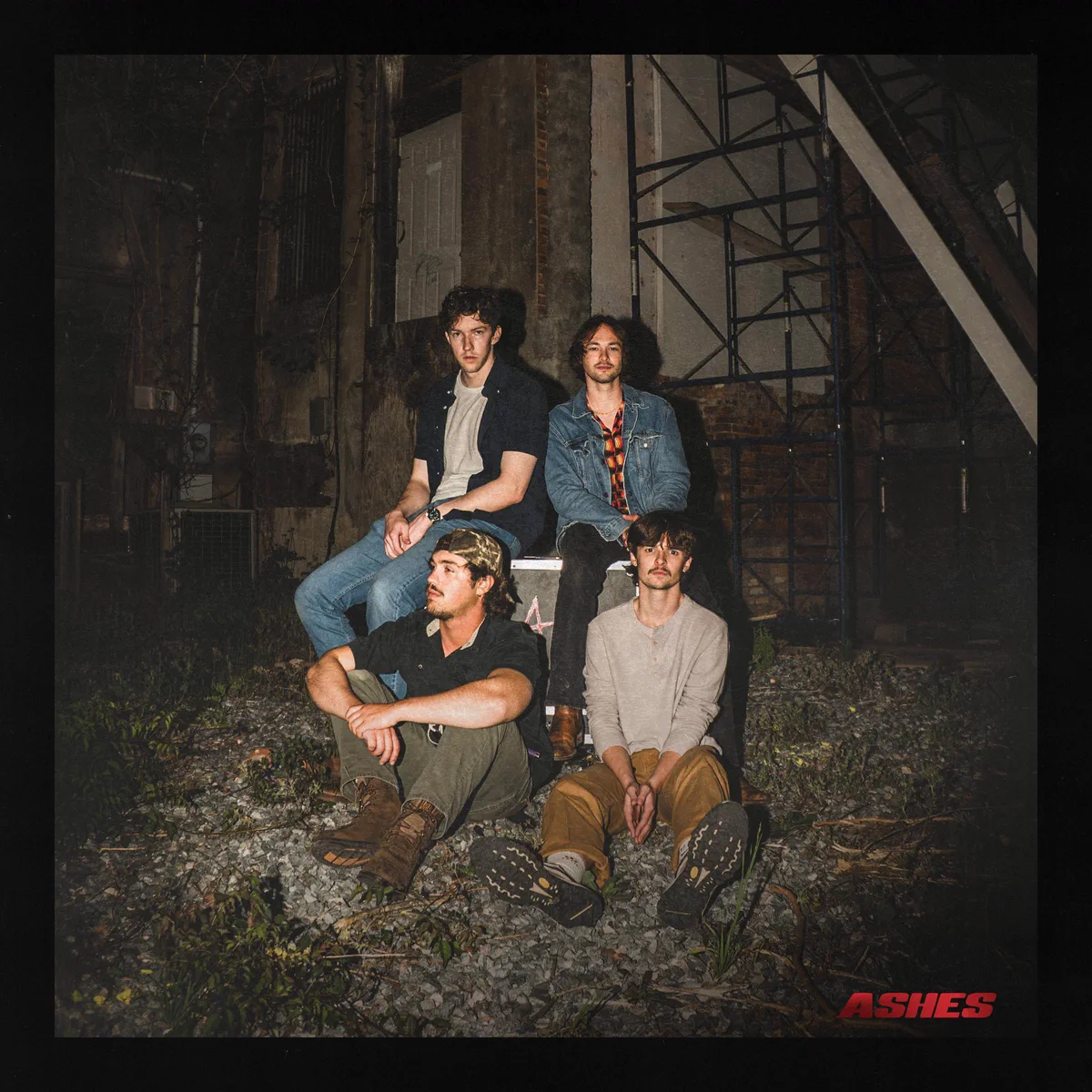 The Ashes EP cover: the four members of ASHES sitting on gravel below a fire escape at night.